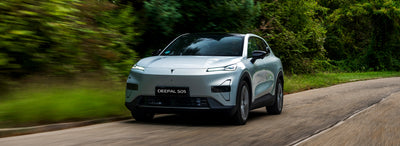 A silver Deepal S05 electric SUV is shown driving on a paved road surrounded by blurred green trees and foliage, indicating a motion shot.